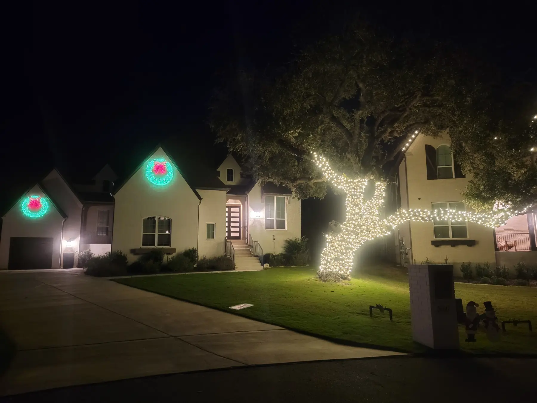 Residential roofline and mature tree illuminated in warm white lights